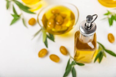 Beyaz dokuya sahip bir şişede zeytin yağı. Zeytin dallı ve meyveli yağ şişesi. Mesaj için yer. kopyalama alanı. Yemek yağı ve salata sosu..