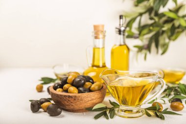 Cam kaselerde zeytinyağı, soslu kayıklar ve dokulu mutfak masasında şişe. Zeytin dallı ve meyveli yağ şişesi. Mesaj için yer. kopyalama alanı. Yemek yağı ve salata sosu. Yakın plan.