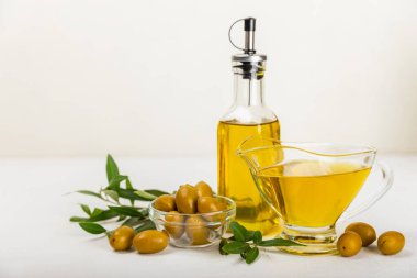 Beyaz dokuya sahip bir şişede zeytin yağı. Zeytin dallı ve meyveli yağ şişesi. Mesaj için yer. kopyalama alanı. Yemek yağı ve salata sosu..