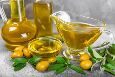 Cam kaselerde zeytinyağı, soslu kayıklar ve dokulu mutfak masasında şişe. Zeytin dallı ve meyveli yağ şişesi. Mesaj için yer. kopyalama alanı. Yemek yağı ve salata sosu. Yakın plan.