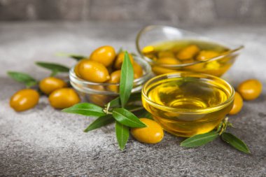 Cam kaselerde zeytinyağı, soslu kayıklar ve dokulu mutfak masasında şişe. Zeytin dallı ve meyveli yağ şişesi. Mesaj için yer. kopyalama alanı. Yemek yağı ve salata sosu. Yakın plan.