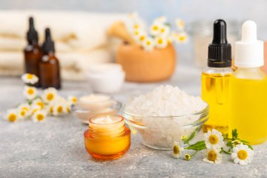 Papatya spası. Papatya çiçekleri, el yapımı sabun, temel yağ kozmetik şişesi, vücut kremi, ovalama ve beyaz desenli deniz tuzu karışımı. Rahatlatıcı güzellik tedavileri. Boşluğu kopyala