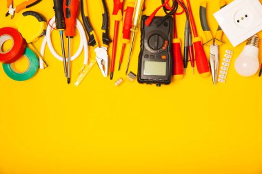 Arka planda elektrikli aletler. Multimetre, inşaat bandı, elektrik bandı, tornavida, pense, otomatik yalıtım striptizcisi, soket ve LED lamba..