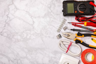 Arka planda elektrikli aletler. Multimetre, inşaat bandı, elektrik bandı, tornavida, pense, otomatik yalıtım striptizcisi, soket ve LED lamba..