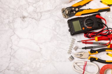 Arka planda elektrikli aletler. Multimetre, inşaat bandı, elektrik bandı, tornavida, pense, otomatik yalıtım striptizcisi, soket ve LED lamba..