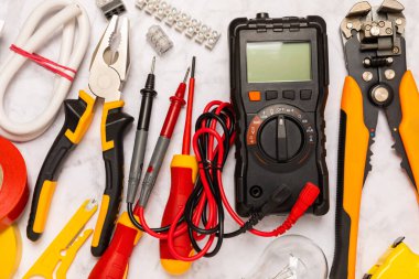 Arka planda elektrikli aletler. Multimetre, inşaat bandı, elektrik bandı, tornavida, pense, otomatik yalıtım striptizcisi, soket ve LED lamba..