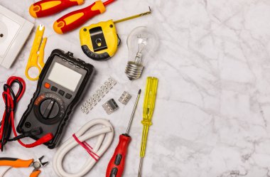 Arka planda elektrikli aletler. Multimetre, inşaat bandı, elektrik bandı, tornavida, pense, otomatik yalıtım striptizcisi, soket ve LED lamba..