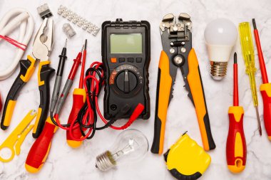 Arka planda elektrikli aletler. Multimetre, inşaat bandı, elektrik bandı, tornavida, pense, otomatik yalıtım striptizcisi, soket ve LED lamba..