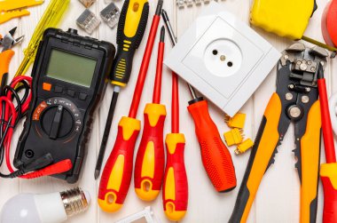 Arka planda elektrikli aletler. Multimetre, inşaat bandı, elektrik bandı, tornavida, pense, otomatik yalıtım striptizcisi, soket ve LED lamba..