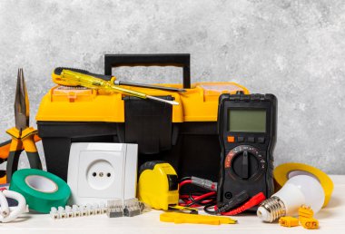 Arka planda elektrikli aletler. Multimetre, inşaat bandı, elektrik bandı, tornavida, pense, otomatik yalıtım striptizcisi, soket ve LED lamba..