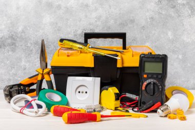 Arka planda elektrikli aletler. Multimetre, inşaat bandı, elektrik bandı, tornavida, pense, otomatik yalıtım striptizcisi, soket ve LED lamba..