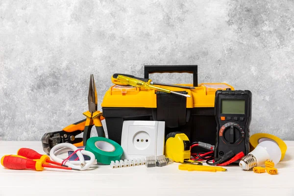 Arka planda elektrikli aletler. Multimetre, inşaat bandı, elektrik bandı, tornavida, pense, otomatik yalıtım striptizcisi, soket ve LED lamba..
