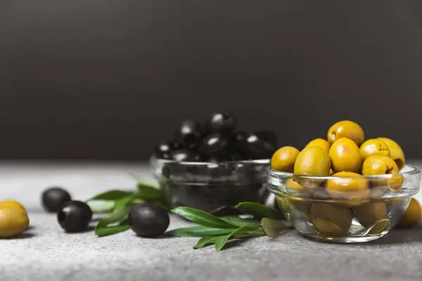 Green and black olives on a textured background. Different types of olives in bowls and olive oil with fresh olive leaves. Delicacy.Mediterranean Kitchen. Copy space.