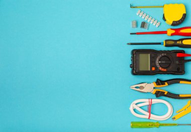 Arka planda elektrikli aletler. Multimetre, inşaat bandı, elektrik bandı, tornavida, pense, otomatik yalıtım striptizcisi, soket ve LED lamba..