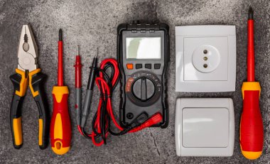 Arka planda elektrikli aletler. Multimetre, inşaat bandı, elektrik bandı, tornavida, pense, otomatik yalıtım striptizcisi, soket ve LED lamba..