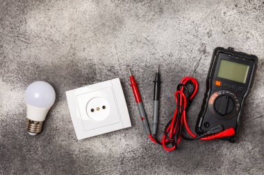 Arka planda elektrikli aletler. Multimetre, inşaat bandı, elektrik bandı, tornavida, pense, otomatik yalıtım striptizcisi, soket ve LED lamba..