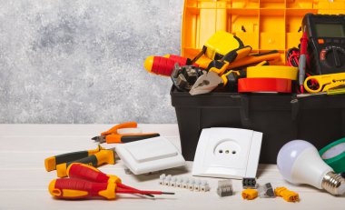 Arka planda elektrikli aletler. Multimetre, inşaat bandı, elektrik bandı, tornavida, pense, otomatik yalıtım striptizcisi, soket ve LED lamba..