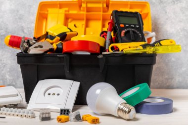 Arka planda elektrikli aletler. Multimetre, inşaat bandı, elektrik bandı, tornavida, pense, otomatik yalıtım striptizcisi, soket ve LED lamba..