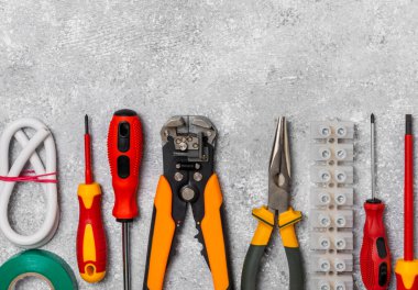 Arka planda elektrikli aletler. Multimetre, inşaat bandı, elektrik bandı, tornavida, pense, otomatik yalıtım striptizcisi, soket ve LED lamba..