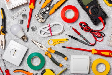 Arka planda elektrikli aletler. Multimetre, inşaat bandı, elektrik bandı, tornavida, pense, otomatik yalıtım striptizcisi, soket ve LED lamba..