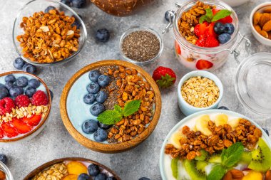 Bir kase granola yoğurt ve dokuma masasında taze böğürtlen. Yoğurt böğürtlen, acai kasesi, spirulina kasesi. Sağlıklı yemek, dengeli kahvaltı. Çilek, yabanmersini, kivi, şeftali, badem ve chia..