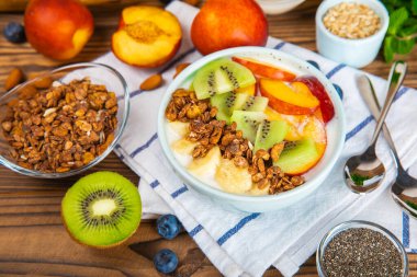 Bir kase granola yoğurt ve dokuma masasında taze böğürtlen. Yoğurt böğürtlen, acai kasesi, spirulina kasesi. Sağlıklı yemek, dengeli kahvaltı. Çilek, yabanmersini, kivi, şeftali, badem ve chia..