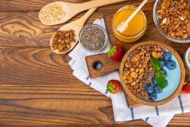 Bir kase granola yoğurt ve dokuma masasında taze böğürtlen. Yoğurt böğürtlen, acai kasesi, spirulina kasesi. Sağlıklı yemek, dengeli kahvaltı. Çilek, yabanmersini, kivi, şeftali, badem ve chia..