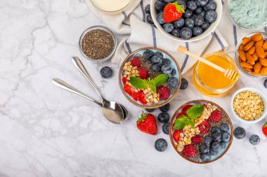 Bir kase granola yoğurt ve dokuma masasında taze böğürtlen. Yoğurt böğürtlen, acai kasesi, spirulina kasesi. Sağlıklı yemek, dengeli kahvaltı. Çilek, yabanmersini, kivi, şeftali, badem ve chia..