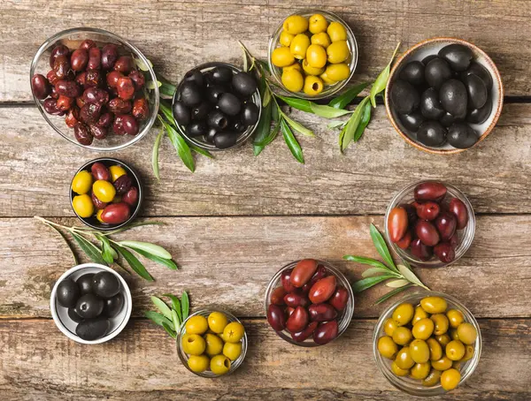 A set of green, red and black olives on  background. Various types of olives in bowls and fresh olive leaves. Vegan. Olive fruits. Place for text. Copy space