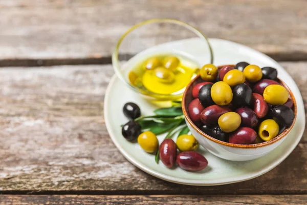 A set of green, red and black olives on  background. Various types of olives in bowls and fresh olive leaves. Vegan. Olive fruits. Place for text. Copy space