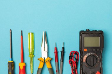 Arka planda elektrikli aletler var. Çoklu metre, inşaat bandı, elektrik bandı, tornavida, pense, otomatik yalıtım striptizcisi, soket ve LED lamba. Düz çizgi. elektrikçi kavramı.