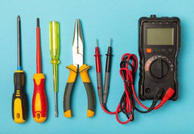 Arka planda elektrikli aletler var. Çoklu metre, inşaat bandı, elektrik bandı, tornavida, pense, otomatik yalıtım striptizcisi, soket ve LED lamba. Düz çizgi. elektrikçi kavramı.