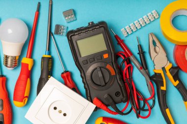 Arka planda elektrikli aletler var. Çoklu metre, inşaat bandı, elektrik bandı, tornavida, pense, otomatik yalıtım striptizcisi, soket ve LED lamba. Düz çizgi. elektrikçi kavramı.