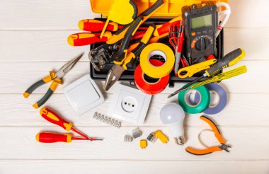 Arka planda elektrikli aletler var. Çoklu metre, inşaat bandı, elektrik bandı, tornavida, pense, otomatik yalıtım striptizcisi, soket ve LED lamba. Düz çizgi. elektrikçi kavramı.