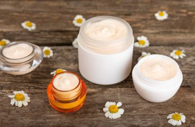 Kahverengi ahşap arka planda papatya çiçekli vücut ve el kremi. Bitki dermatolojik kozmetik hijyen kremi. Doğal kozmetik ürünü. Kozmetik tüpü. Ekolojik kozmetik. Uzayı kopyala.