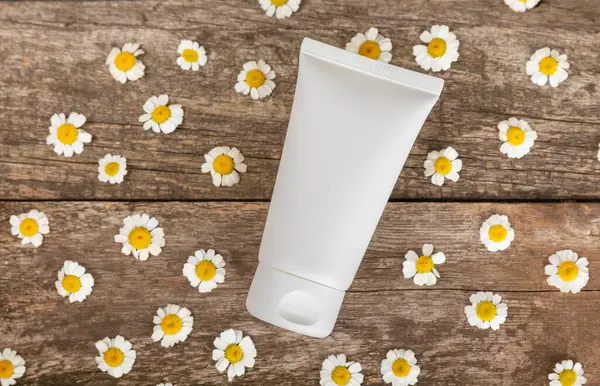 Body and hand cream with chamomile flower on a brown wooden background. Herbal dermatological cosmetic hygiene cream. Natural cosmetic product. Cosmetic tube. Ecological cosmetics.Copy space.