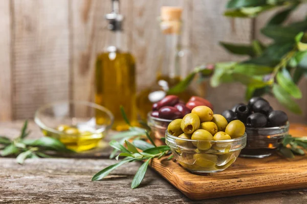 A set of green, red and black olives on  background. Various types of olives in bowls and fresh olive leaves. Vegan. Olive fruits. Place for text. Copy space.