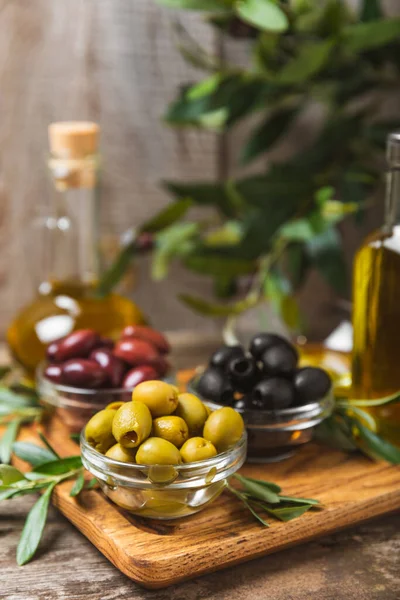 A set of green, red and black olives on  background. Various types of olives in bowls and fresh olive leaves. Vegan. Olive fruits. Place for text. Copy space.