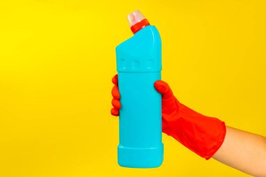 Sarı arka planda temiz kimyasalla dolu bir şişeyi tutan kırmızı plastik eldivenli bir temizlikçinin eli. Ticari temizlik şirketi. Bahar temizliği. Metin veya logo için boşluk.