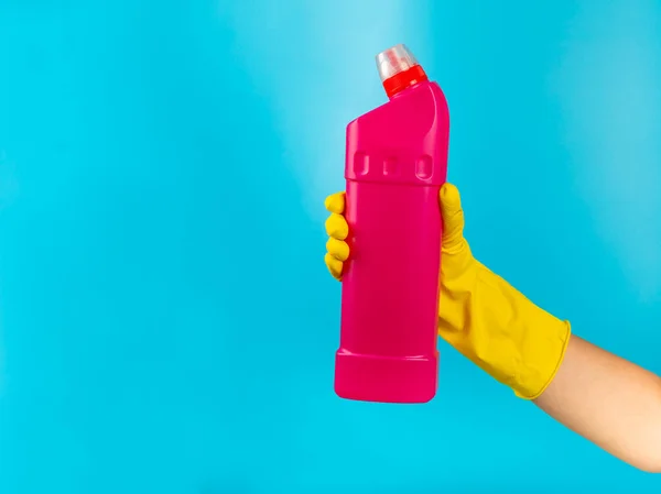 A cleaner\'s hand in a yellow rubber protective glove holding a bottle with a cleaning chemical on a blue background. Commercial cleaning company. Spring regular cleaning. Space for text or logo.