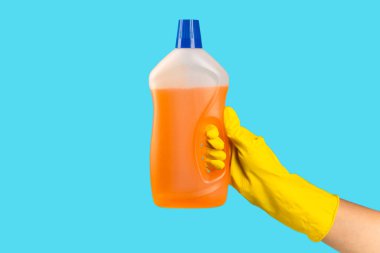 Sarı lastik koruyucu eldivenli bir temizlikçinin elinde mavi arka planda temizleyici kimyasalı olan bir şişe var. Ticari temizlik şirketi. Bahar temizliği. Metin veya logo için boşluk.
