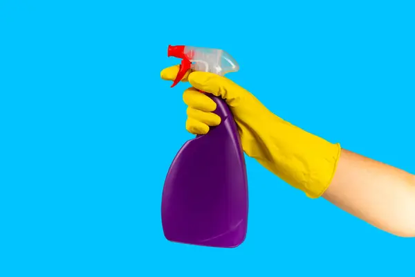 A cleaner\'s hand in a yellow rubber protective glove holding a bottle with a cleaning chemical on a blue background. Commercial cleaning company. Spring regular cleaning. Space for text or logo.