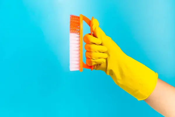 Brush for cleaning in hand. Women\'s hand cleaning on a colored background. Cleaning or housekeeping concepts.