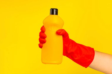 Sarı arka planda temiz kimyasalla dolu bir şişeyi tutan kırmızı plastik eldivenli bir temizlikçinin eli. Ticari temizlik şirketi. Bahar temizliği. Metin veya logo için boşluk.