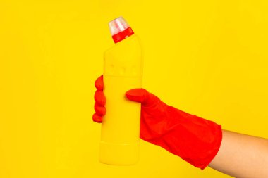 Sarı arka planda temiz kimyasalla dolu bir şişeyi tutan kırmızı plastik eldivenli bir temizlikçinin eli. Ticari temizlik şirketi. Bahar temizliği. Metin veya logo için boşluk.