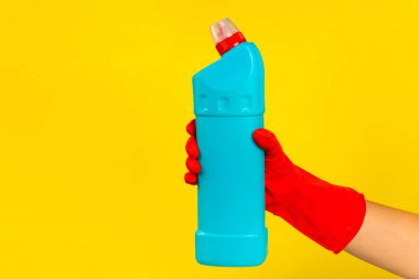 Sarı arka planda temiz kimyasalla dolu bir şişeyi tutan kırmızı plastik eldivenli bir temizlikçinin eli. Ticari temizlik şirketi. Bahar temizliği. Metin veya logo için boşluk.