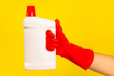 Sarı arka planda temiz kimyasalla dolu bir şişeyi tutan kırmızı plastik eldivenli bir temizlikçinin eli. Ticari temizlik şirketi. Bahar temizliği. Metin veya logo için boşluk.