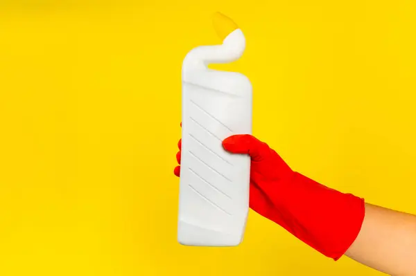 A cleaner\'s hand in a red rubber protective glove holding a bottle with a cleaning chemical on a yellow background. Commercial cleaning company. Spring regular cleaning. Space for text or logo.