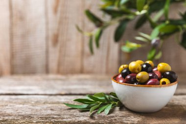 Yeşil, siyah ve kırmızı zeytinler, kahverengi ahşap arka planda zeytin yağı. Bir kâse taze zeytin ve taze zeytin yaprakları. Vejetaryen. Zeytin meyveleri. Mesaj için yer. Boşluğu kopyala.