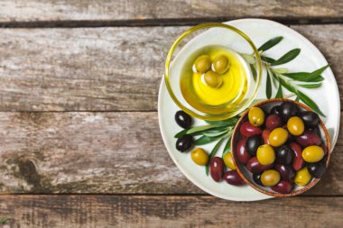 Yeşil, siyah ve kırmızı zeytinler, kahverengi ahşap arka planda zeytin yağı. Bir kâse taze zeytin ve taze zeytin yaprakları. Vejetaryen. Zeytin meyveleri. Mesaj için yer. Boşluğu kopyala.